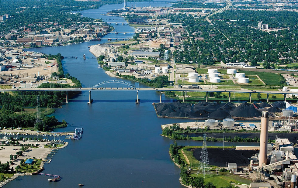 Aerial view of a wide river through an industrial city, with bridges, white storage tanks, black coal piles, and green neighborhoods. Green Bay Wisconsin