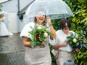 Bridesmaids arrive joyfully under umbrellas, braving the winter chill at a wedding in Blazing Donkey, Kent.