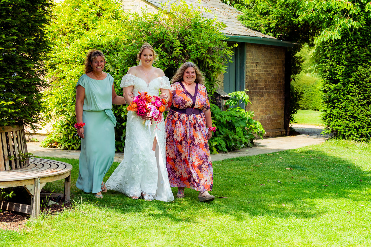 3 women walking, the woman in the middle is dressed in a wedding dress