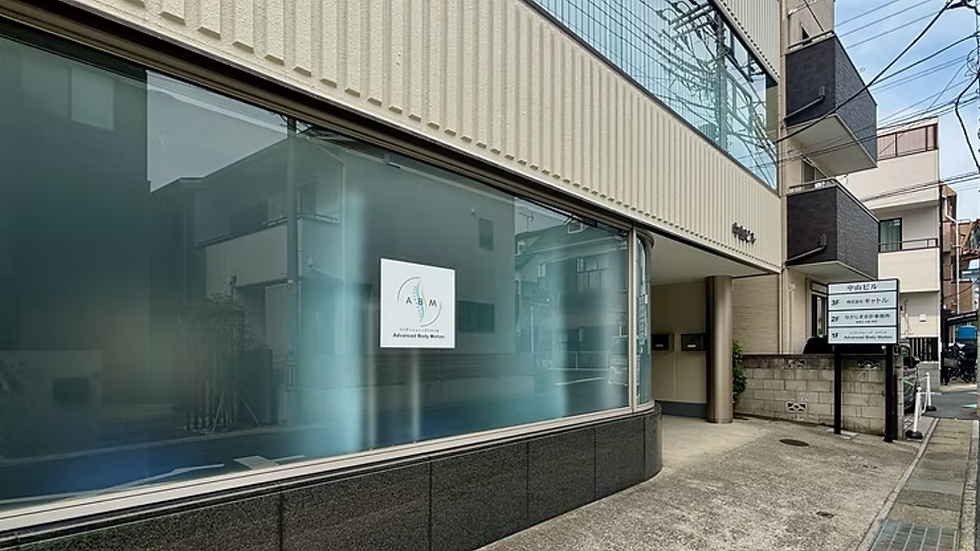 「アドバンスドボディモーション大宮コンディショニング整体」が入るビルの外観。窓にロゴと店舗名が貼られている。