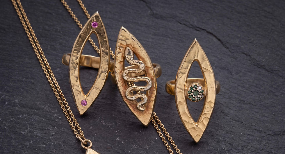 Three golden Vesica Piscis shaped rings. One with a serpent moving up the middle, one with a pink sapphire set at each point, one with a blue diamond iris and a black diamond pupil.