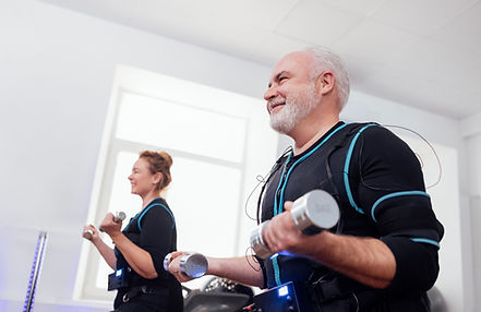 Older smiling couple in ems suits doing electrical muscle stimulation workout with dumbbel