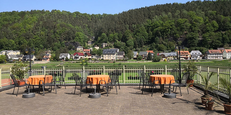 Ein Bildausschnitt der Terrasse der Elbaussicht - Krippen mit Tischen und Stühlen und einem Ausblick auf das gegenüber liegende Ufer