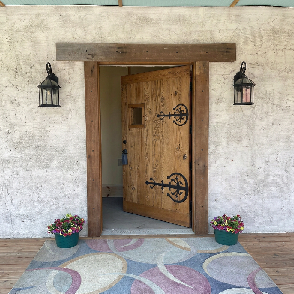 Front entrance of straw bale home with wooden door, decorative hinges, porch lights, and colorful flower pots