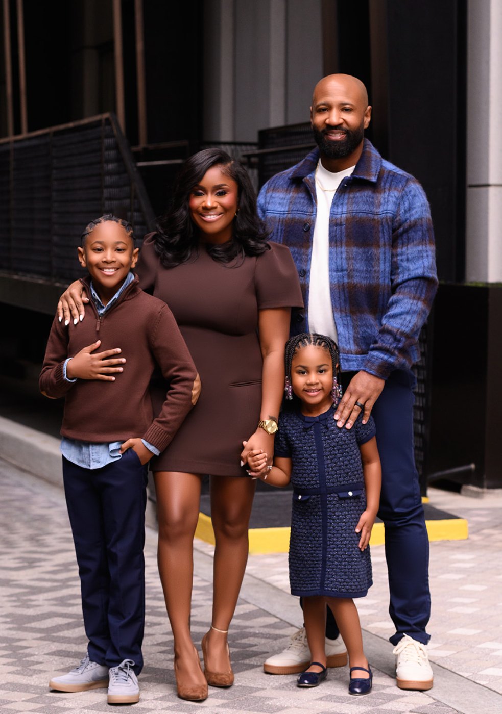 Family of four in coordinated brown and navy smiling together on a city sidewalk
