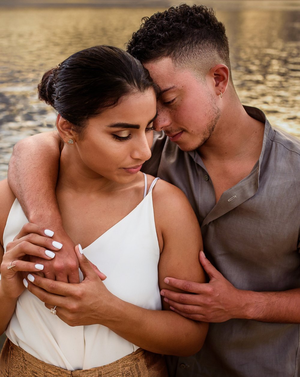 Couple resting forehead to forehead in a close embrace beside golden, sunlit water
