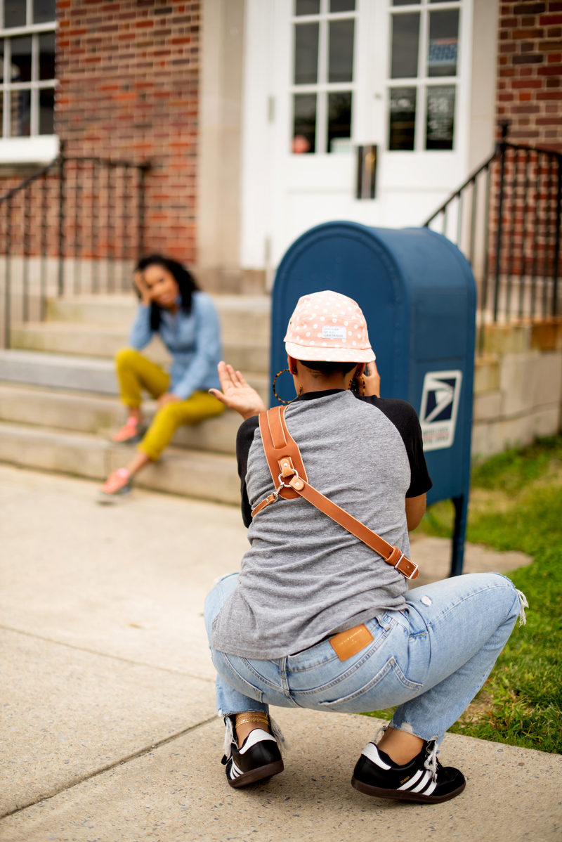 Ashleigh crouched on a sidewalk with her camera, directing a smiling woman seated on brick steps beside a blue mailbox