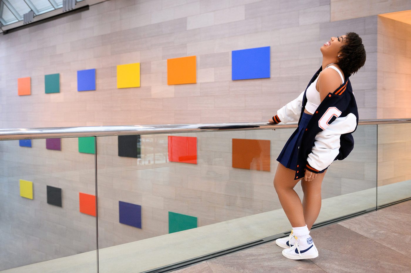 Senior in a varsity jacket laughing with her head tipped back beside a wall of colorful squares