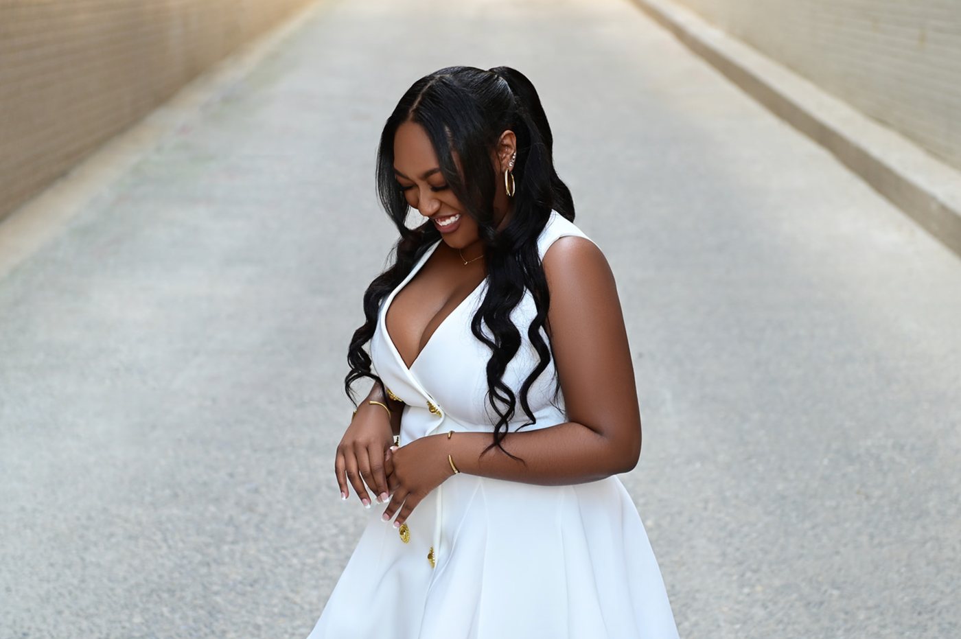 Senior in a white tailored dress with gold buttons laughing in a sunlit alley