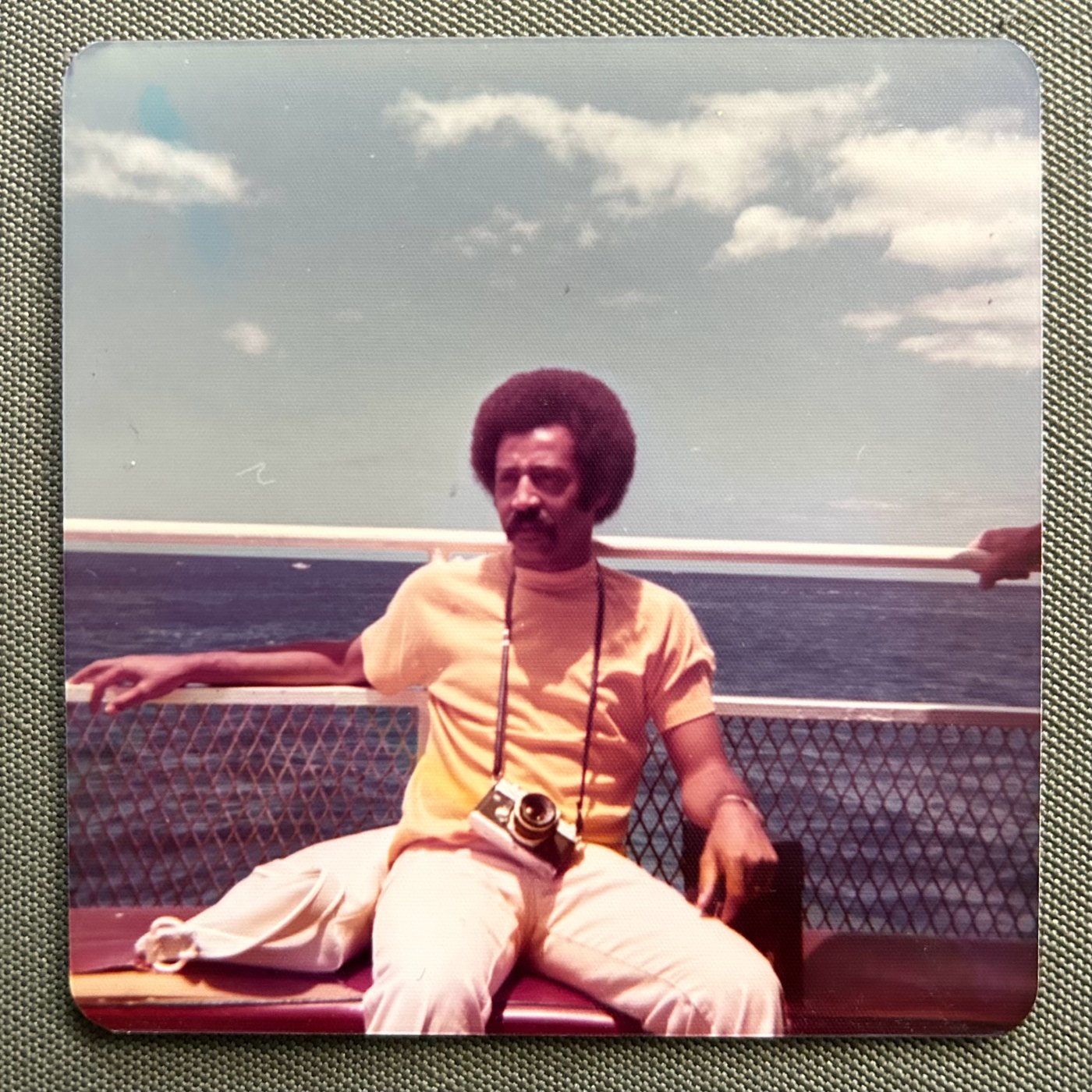 Vintage snapshot of Ashleigh’s dad on a ferry deck, a camera hanging from a strap around his neck