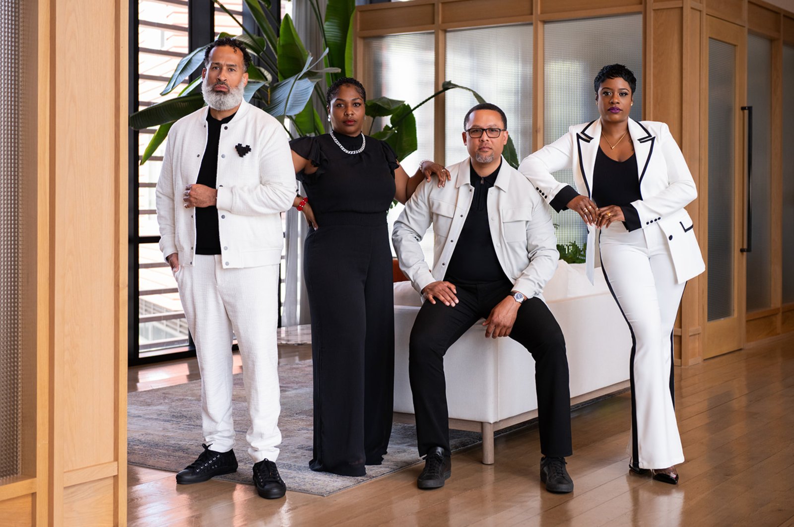 Four team members in coordinated black and white outfits posed in a modern wood-paneled office lounge
