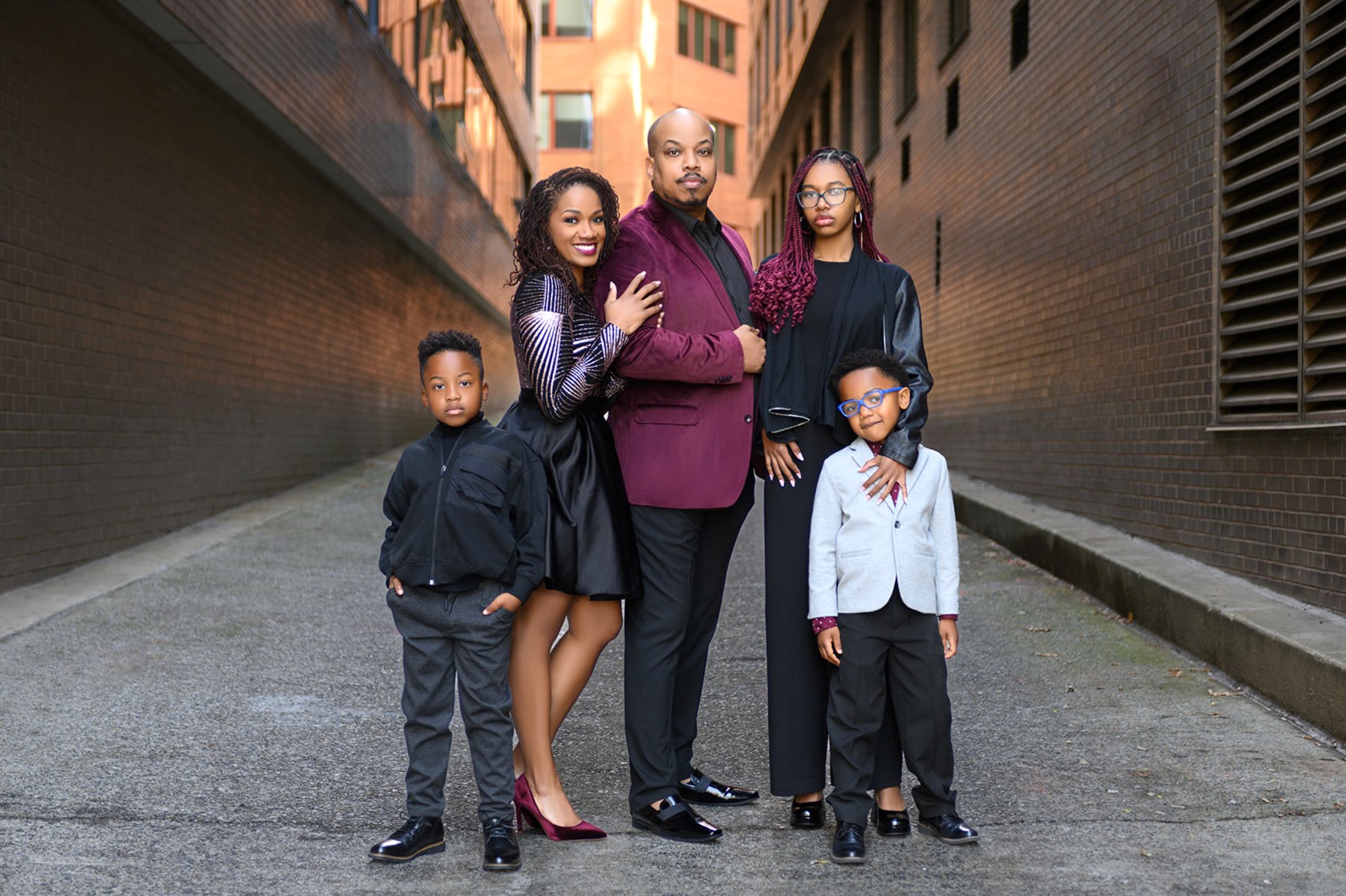Family of five in coordinated burgundy, black, and gray standing together in a city alley