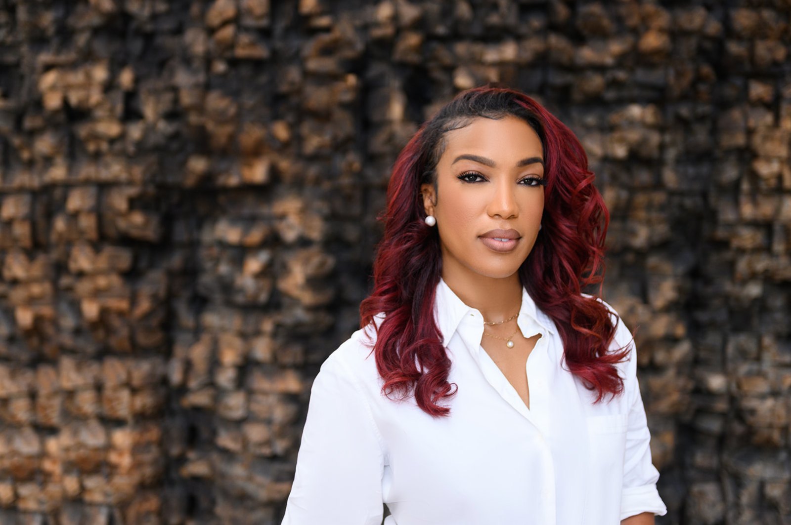 Woman with red waves in a crisp white shirt in front of a textured wood wall