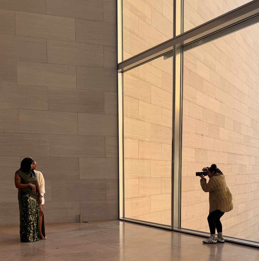 Ashleigh photographing a couple beside a tall stone wall and window in a sunlit gallery