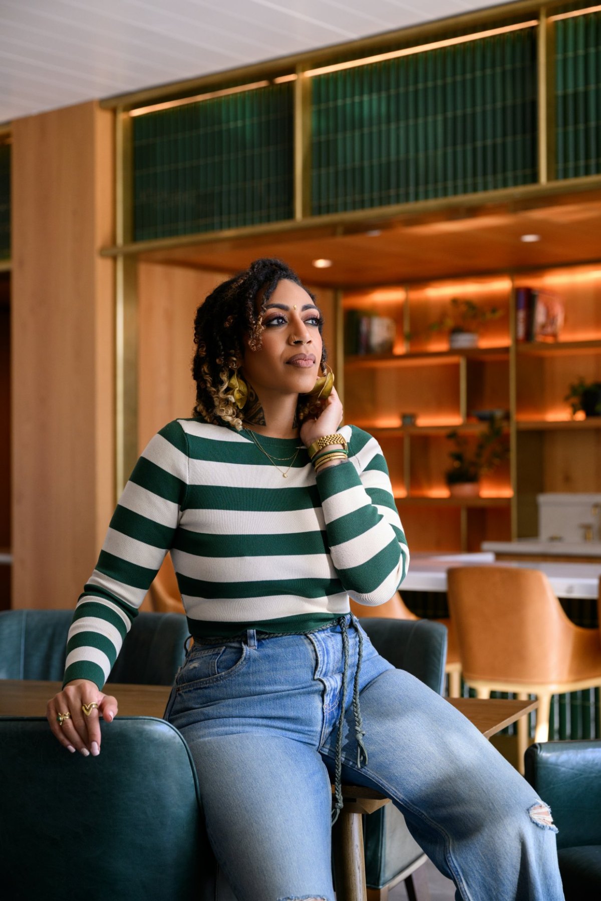 Ashleigh Bing in a green and cream striped sweater, seated in a warm wood-paneled lounge