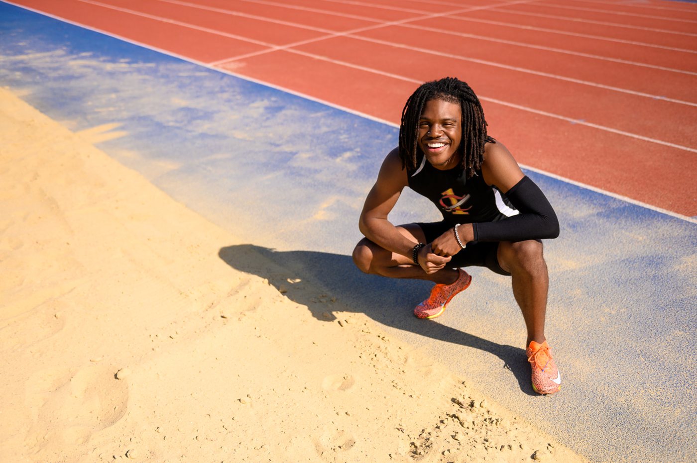 Track athlete crouching beside the long-jump sand pit with the red track behind him