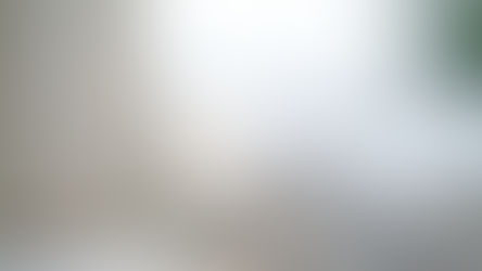Fluffy, clean, white bed surrounded by white curtains and a umbrella bedside lamp on a table