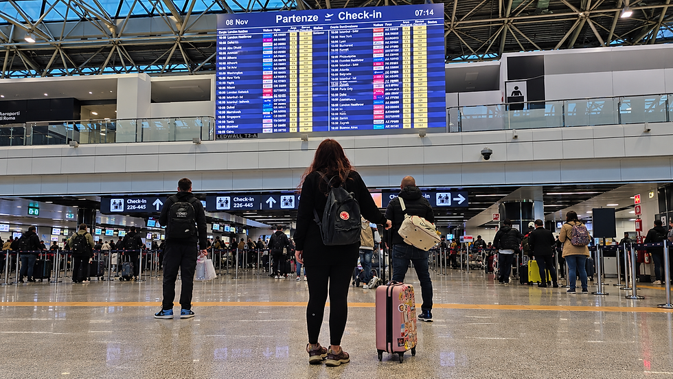 Mujer con maleta frente a panel de vuelos en aeropuerto.