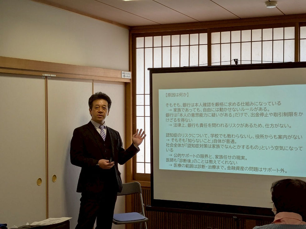 認知症による資産凍結リスクの背景を解説する講師と、表示されたスライド資料