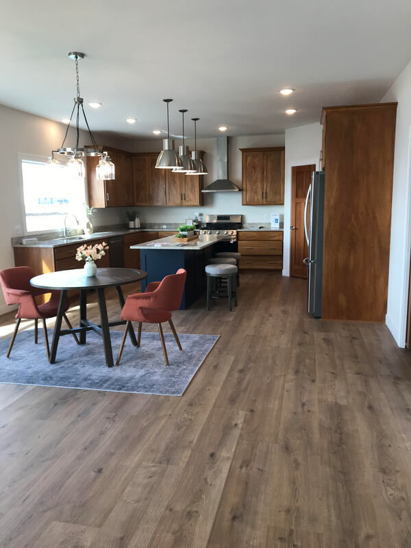 Image of kitchen and casual dining room open to living room. Includes cherry cabinets, large window over kitchen sink, and a navy blue over-sized center island with granite top, storage underneath, and pendant lighting above.
