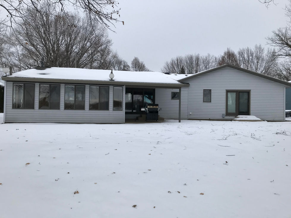 Features an image of the lakeside view of the home before the remodel/addition. Includes white siding, three-season porch, and a few small, brown windows.