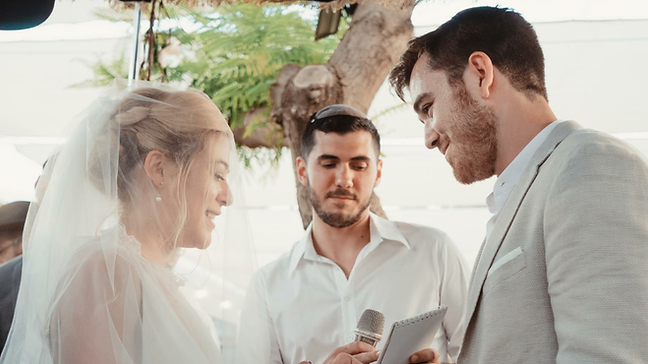 Rabbi Daniel Reichenbach officiates as a couple exchanges rings beneath a chuppah.