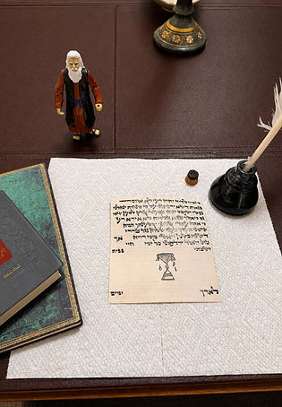 A scribal workspace with Hebrew lettering on parchment, a quill and inkpot, books, and a small Moses figurine.