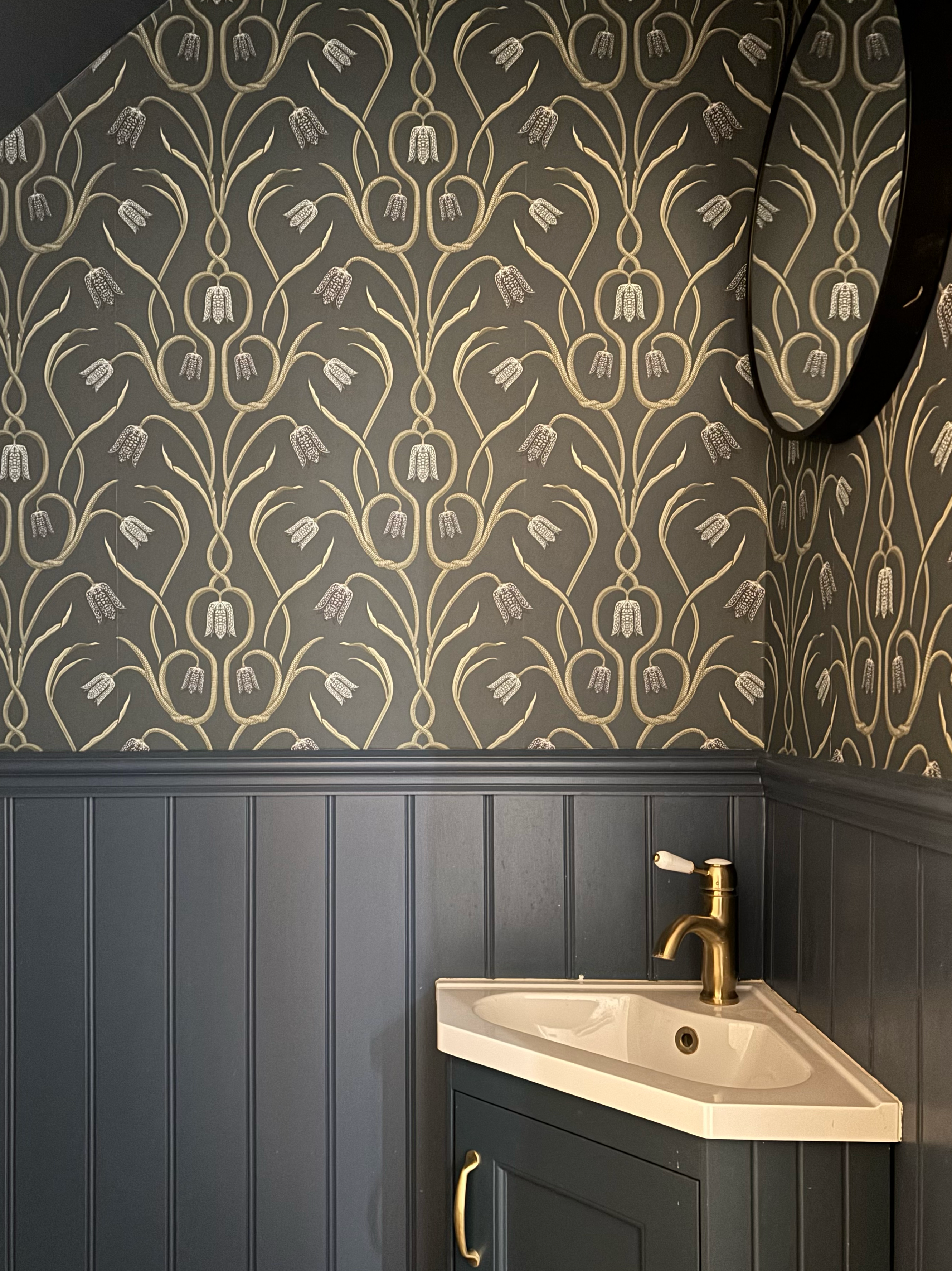 Serpent Vine wallpaper in midnight blue with green botanical vines in a cloakroom with dark panelling and brass tap