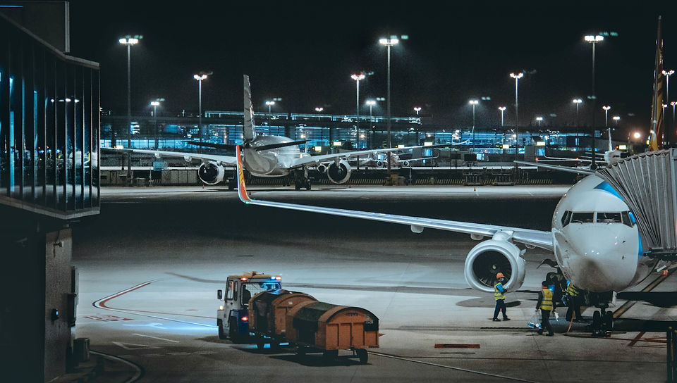 Personale di terra traina un carrello merci accanto a un aereo sul piazzale illuminato di notte