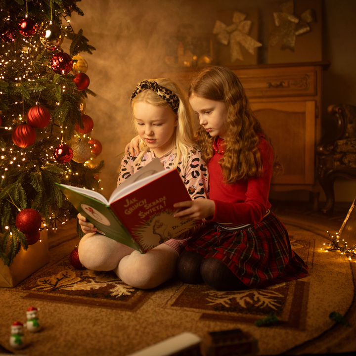 Two girls sitting beside a Christmas tree and reading a festive book