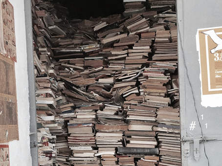 Puerta abierta a la calle completamente bloqueada por pilas de libros apilados hasta el techo, sin orden ni espacio para entrar.