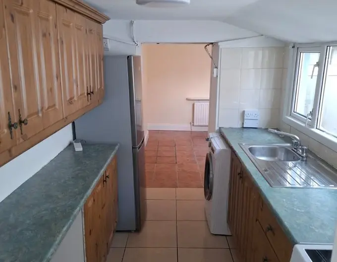 The kitchen at 6Maymount Villas, with wood cabinets and green marble-style countertops on either side of the kitchen, a large American-size fridge-freexer, washing machine, large double windows over the sink, and stove.