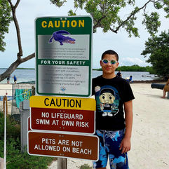 A teen smiling next to "Caution Alligators" swim warning sign at John Pennekamp Coral Reef State Park