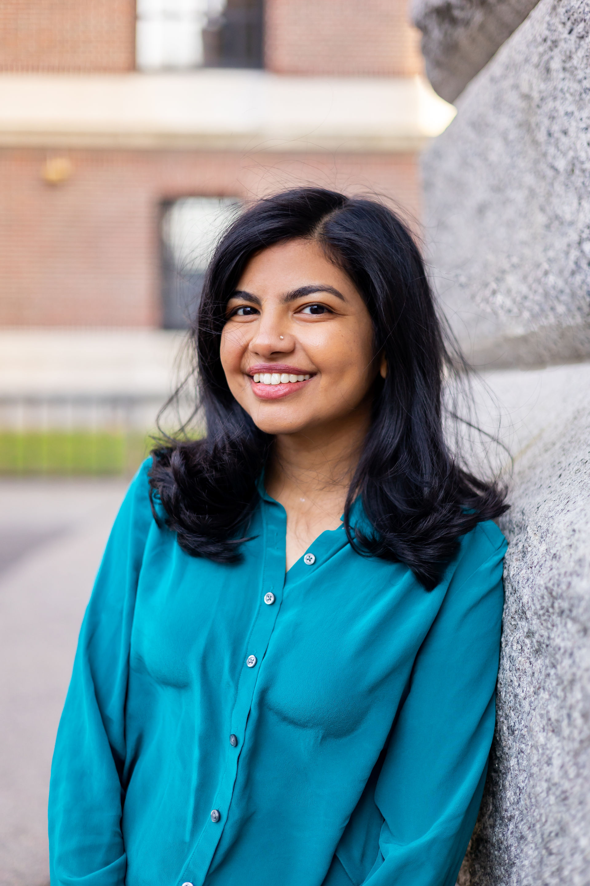 Young Indian Woman wearing a teal shirt leaning against a building at Harvard