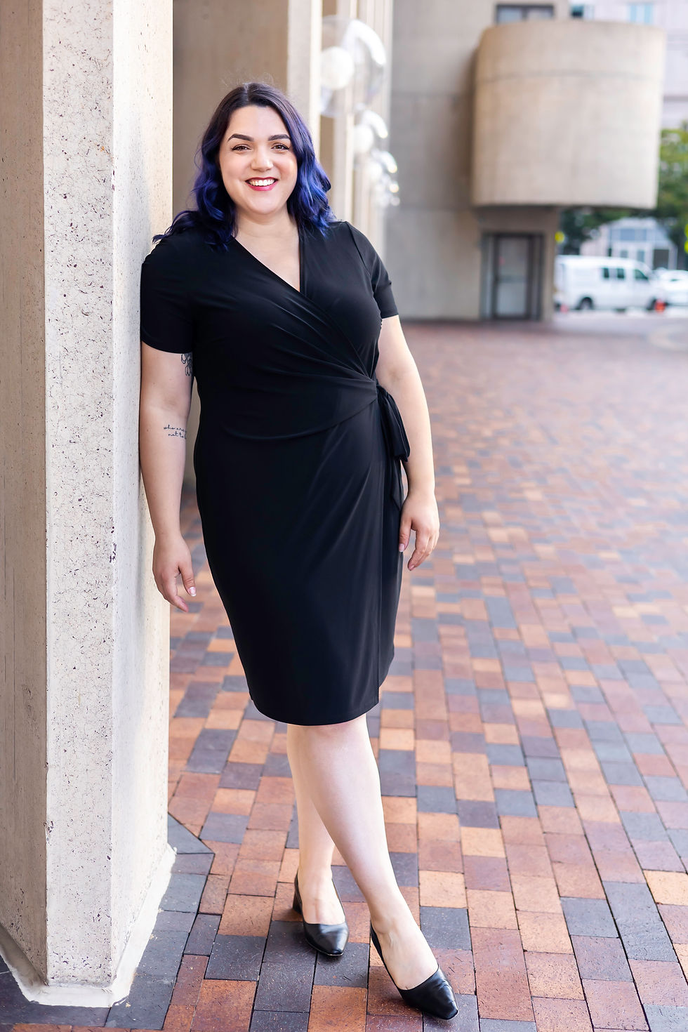 Headshot of soprano Rose Lewis with blue hair wearing a black dress leaning against a pillar