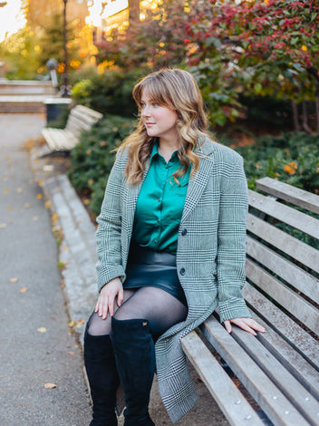 A woman in a green shirt and black skirt seated on a bench at the Boston Public Garden looking off to the left.