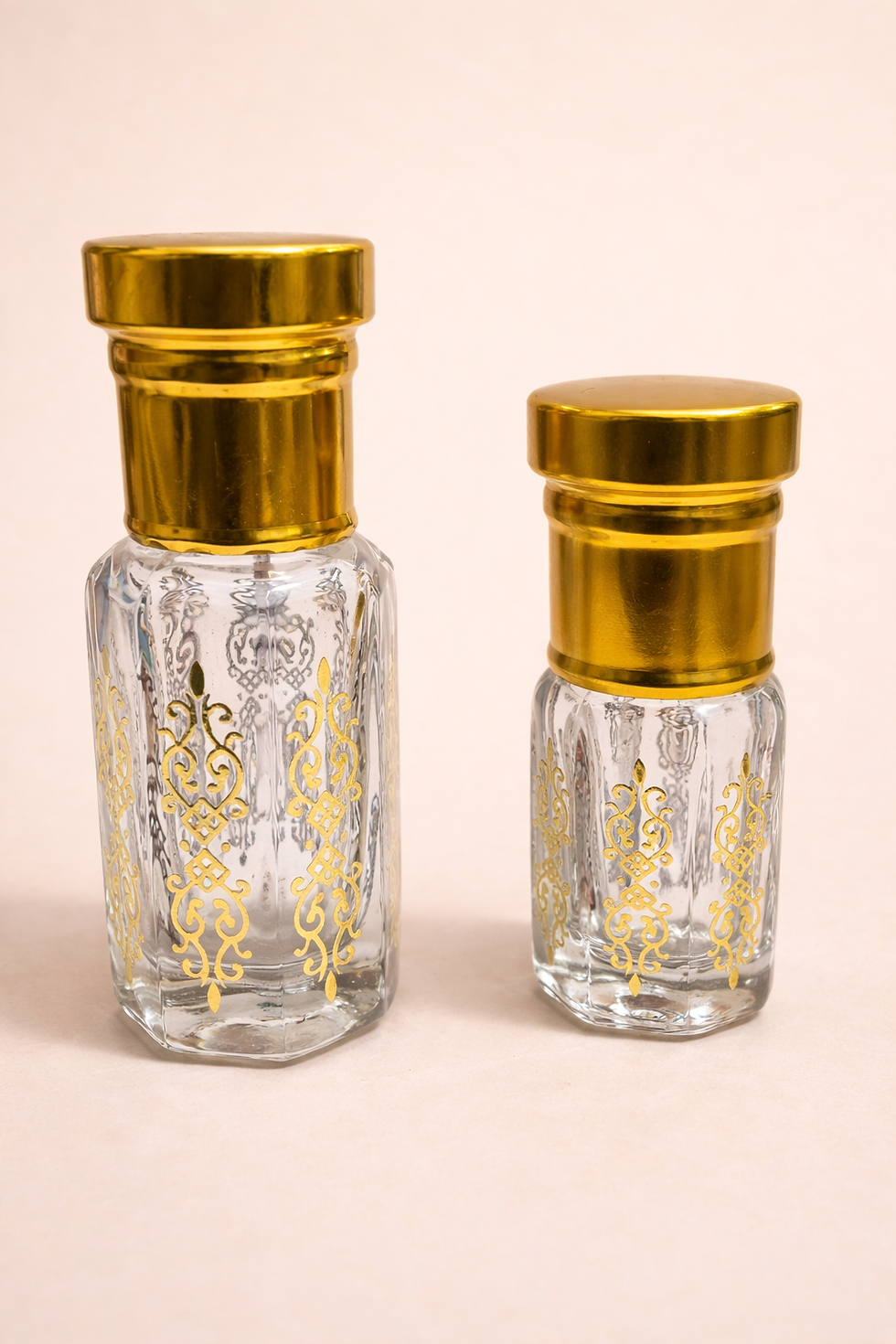 Two clear glass bottles with gold caps and patterns