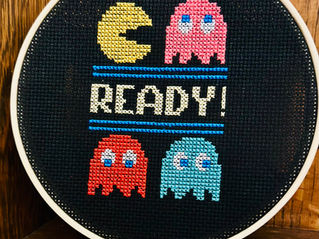 Pac-Man characters cross stitched onto black fabric with a wooden hoop