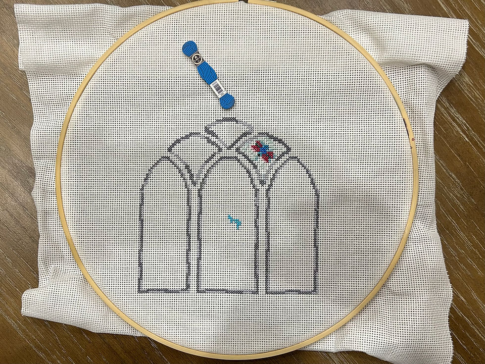 A cross stitch hoop with part of a stained glass window stitched on white embroidery fabric.