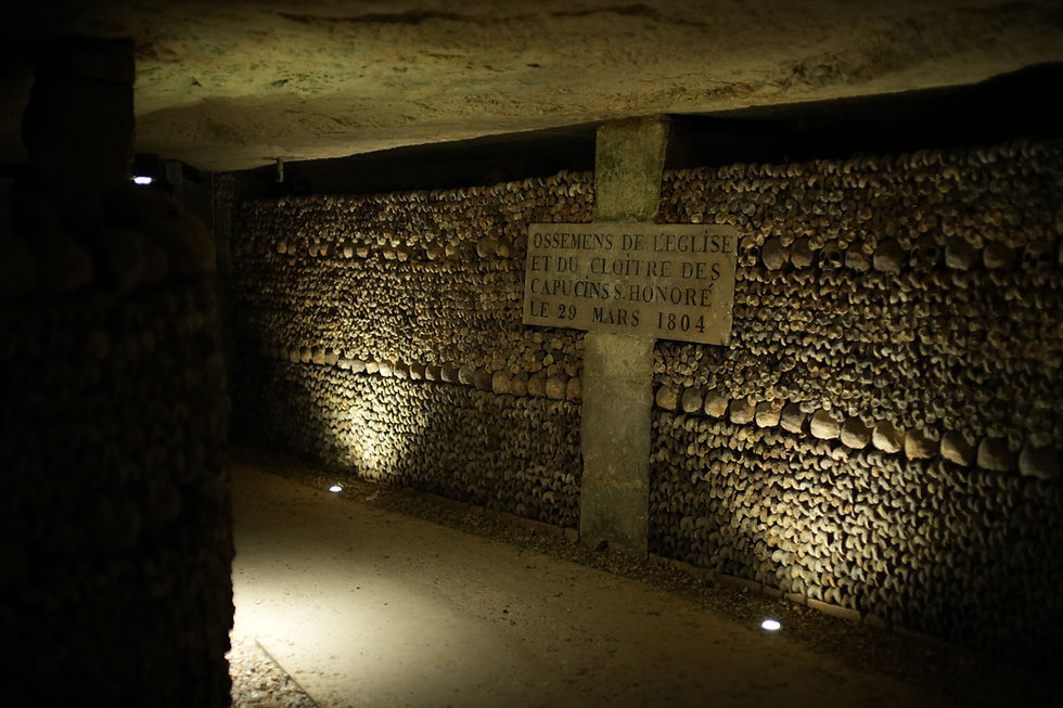 Dimly lit underground ossuary with walls of bones and a French sign reading Ossements de l’église et du cloître des Capucins, 1804