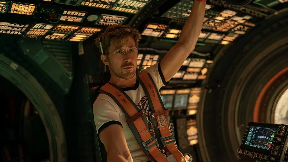 Man in a spacecraft cockpit, wearing a harness and glasses, raises one arm near glowing controls with a focused look.