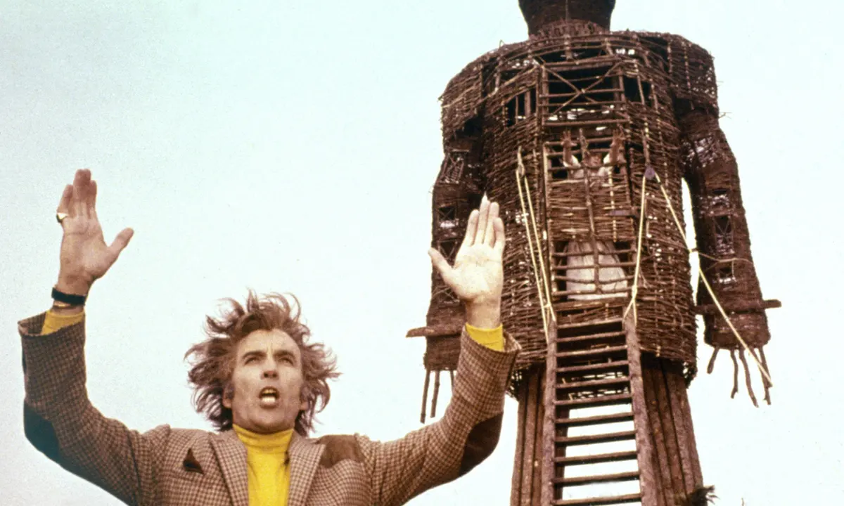 A man stands in front of a burning wicker man