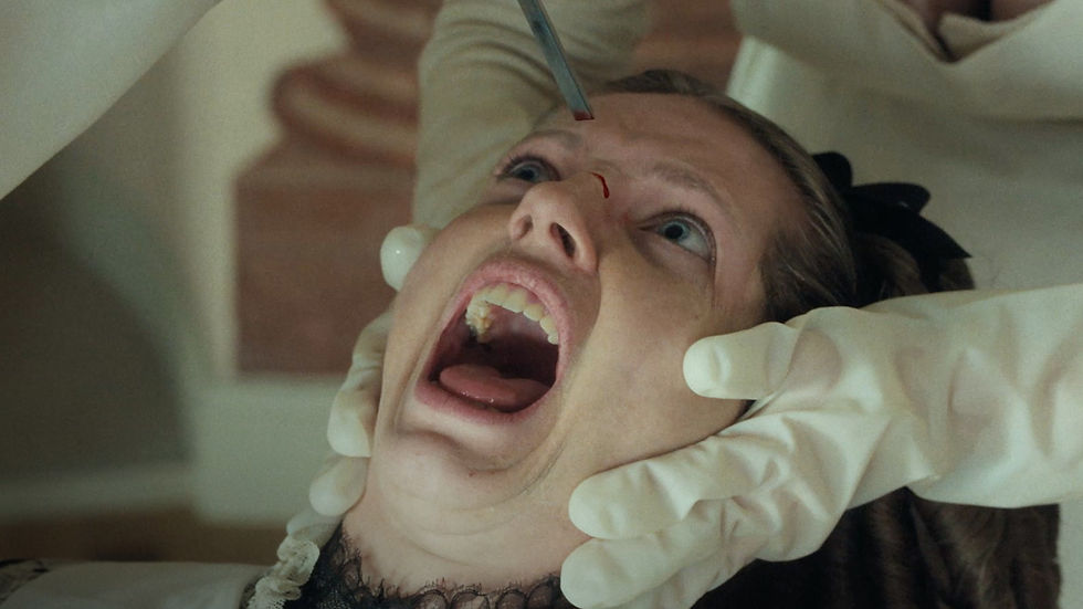 A person with a facial expression of fear is held by gloved hands, while a metallic tool touches their forehead in a clinical setting.