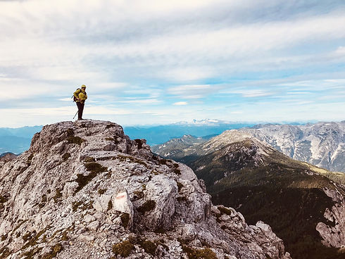 Ein Wanderer steht im Toten Gebirge auf einem Felsen. Im Hintergrund ist der Hohe Dachstein erkennbar.