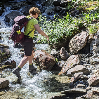 Claudia Fröhlich, die Bergwanderführerin, quert einen kleinen Bach und steigt auf Steinen.