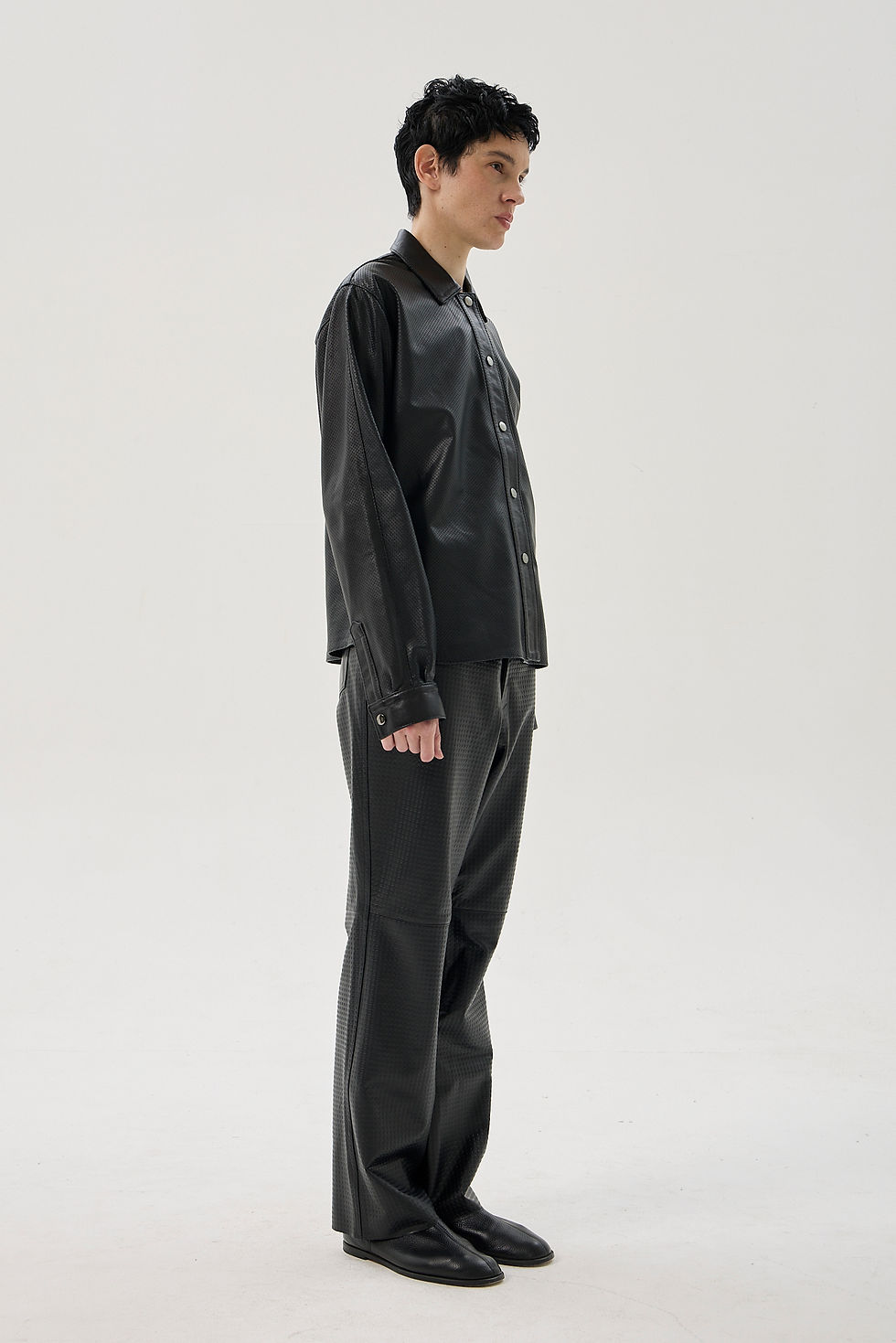 Black perforated sheepskin shirt with a classic collar, front snap closure, and curved hem