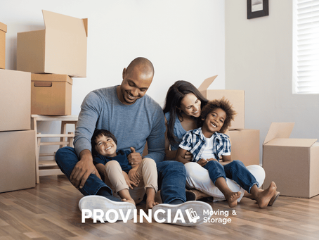 Happy family with two children sitting among moving boxes in their new home, showing a successful moving with kids experience.