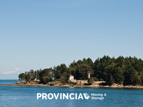 Scenic waterfront view of Mayne Island, featuring calm ocean water, forested shoreline, coastal homes, and a lighthouse under a clear blue sky.