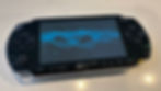 Black Sony PSP showing the TRAX ribbons visualization, blue curves of light on a dark screen