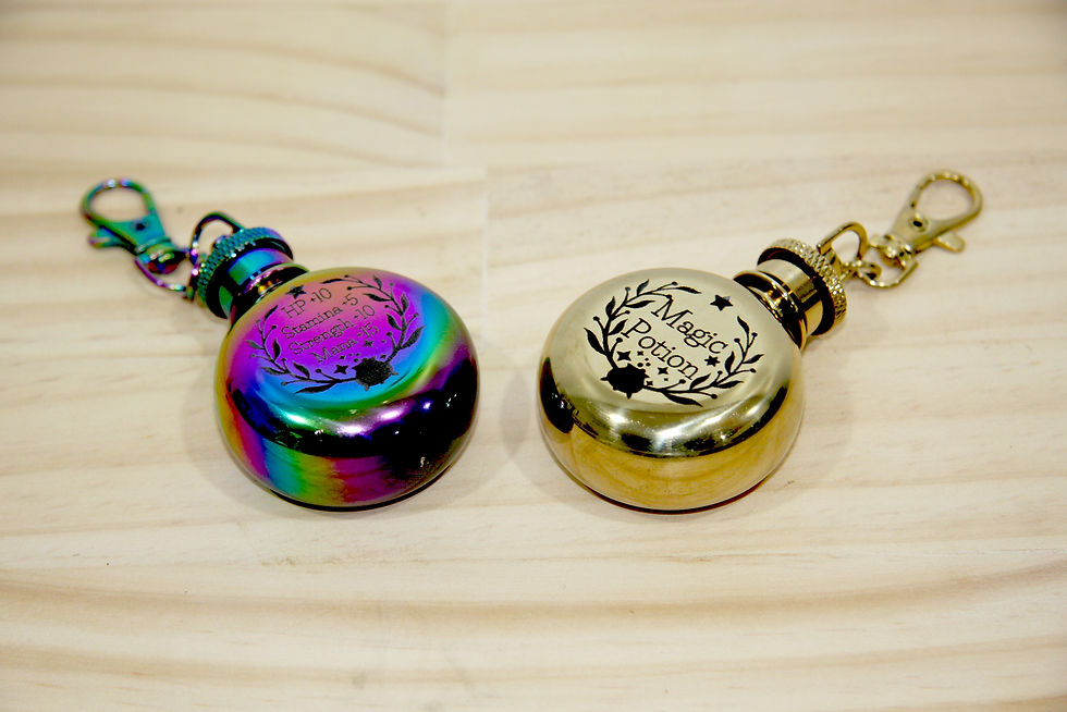 Thumbnail: Cute Magic Potion Engraved 1oz Tiny Keychain gold and multicolored Rainbow Flask on a wood benchtop